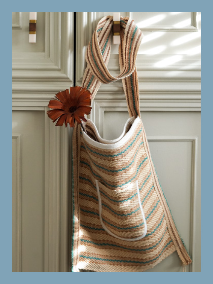 A beautiful bag hanging from a door handle with a flower in it