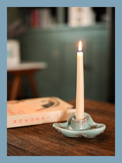 A ceramic candle holder with a tall candle next to a book of Hokusai's art