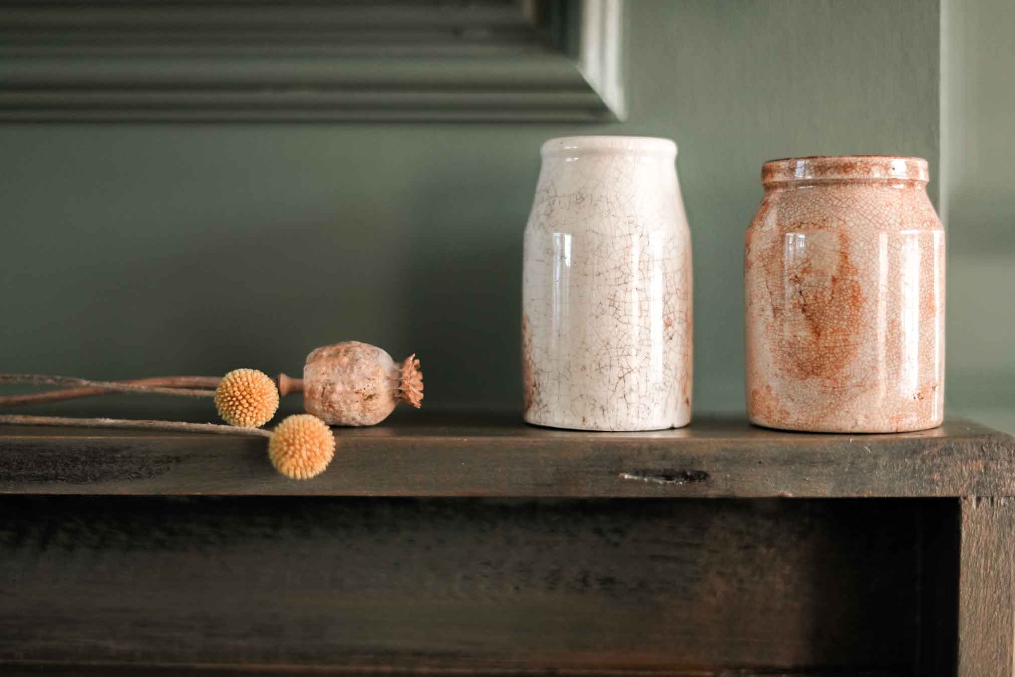 Ceramics on a fireplace near some dried poppy flowers