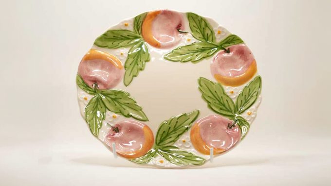 A Bordallo ceramic plate with hand painted leaves and peaches in light pink