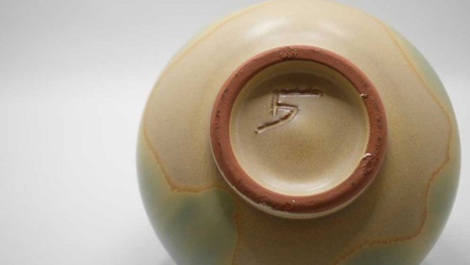 The underside of a pot marked with a 5 A blue and cream pot with a puzzle like lid that fits to the base