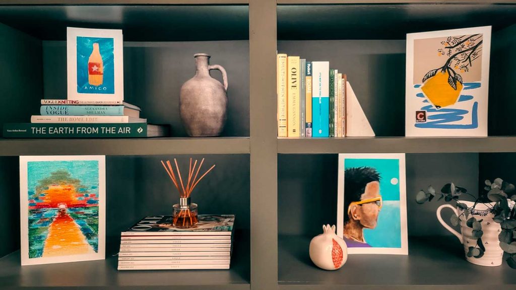 A LIBRARY SHELF WITH ART CARDS IN VARIOUS SIZES AND STYLES ON THE SHELVES SURROUNDED BY BOOKS AND MAGAZINES.